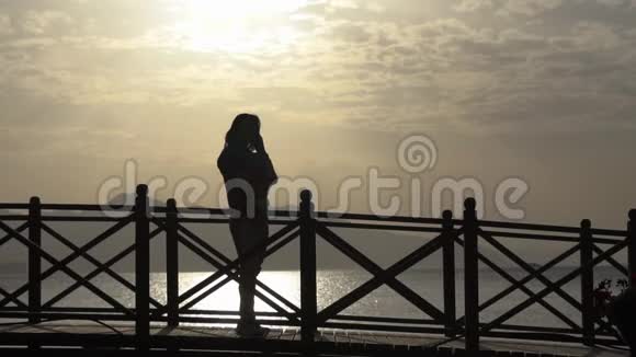 女孩在打电话在日出时站在桥上慢动作视频的预览图