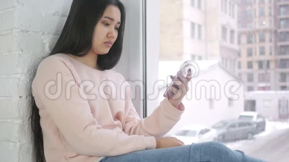 年轻的亚洲女性震惊地看着智能手机视频的预览图