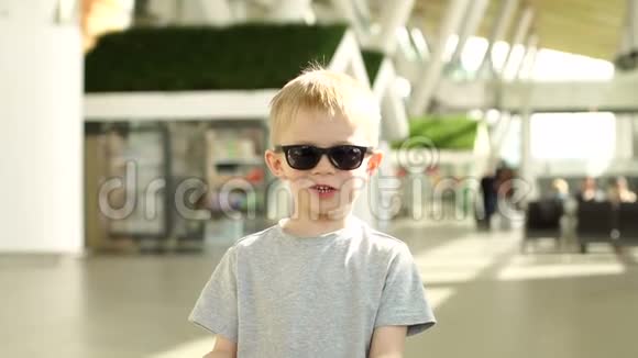 机场大楼里一个微笑的小男孩戴着太阳镜的肖像视频的预览图