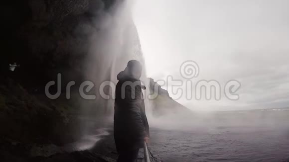 年轻的游客拿着自拍棒在冰岛的gopro相机上拍摄强大的瀑布Seljalandsfoss视频的预览图