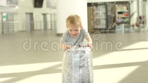 一个活泼开朗的小男孩在候机室的机场玩一个手提箱视频的预览图