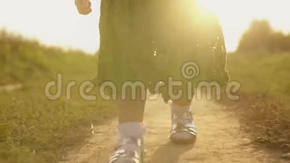 在一个阳光明媚的日子里stadicam拍摄了一个女孩走在农村的田野小路上双脚特写镜头视频的预览图