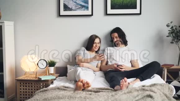 丈夫和妻子用智能手机笑着坐在家里的床上视频的预览图