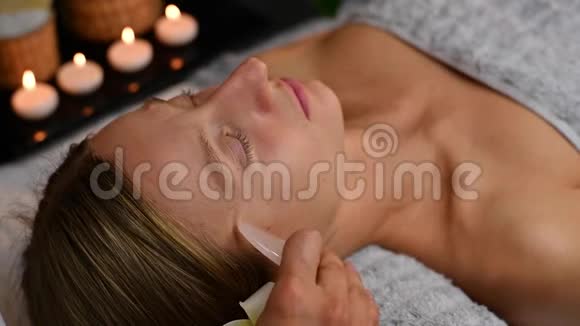 美容师用玉石做专业的面部按摩在水疗中心接受面部按摩的妇女视频的预览图