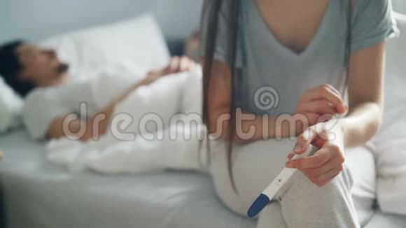 紧张的女人抱着妊娠试验阳性结果而男人睡在床上视频的预览图