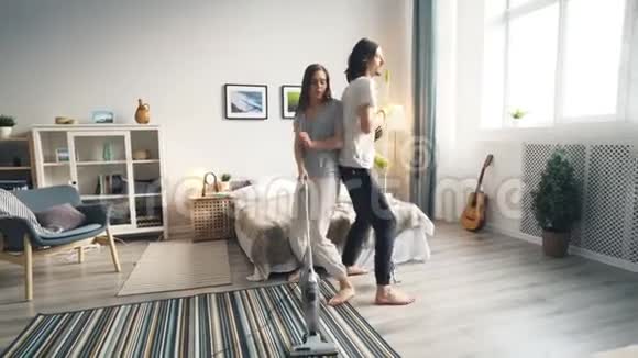 男人和女人在家里打扫地板用拖把和吸尘器玩视频的预览图