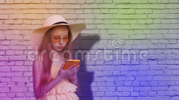 少女在砖墙背景上浏览手机色彩斑斓年轻女孩用智能手机冲浪视频的预览图