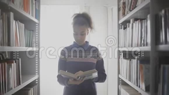 年轻卷曲的非洲裔美国妇女正在看书而走在图书馆的书架之间视频的预览图