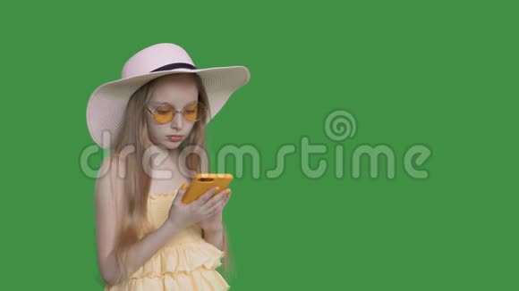 穿黄色连衣裙和太阳镜的年轻女孩在透明的绿色背景上使用手机夏天的少女视频的预览图