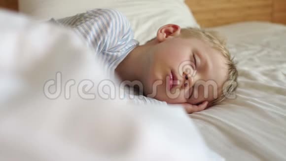一个金发小男孩睡在一张白色的床上慢动作视频的预览图