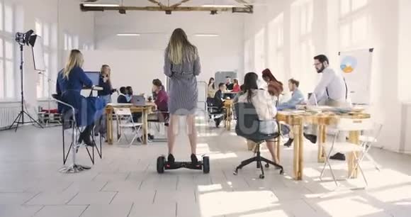 镜头跟随自信的女领导使用电动滑板车在现代阁楼办公室周围移动健康的工作场所视频的预览图