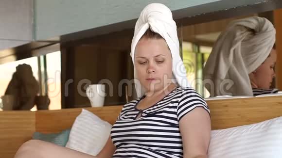 一个坐在床上头上戴着毛巾的女人用有线电话交谈视频的预览图