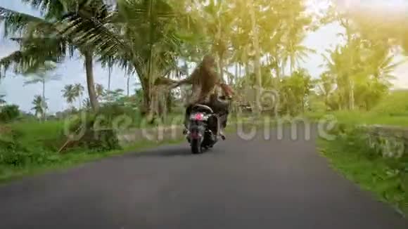 日落时分一对幸福的夫妇在热带公路上骑摩托车绊倒户外拍摄的年轻夫妇骑摩托车男子视频的预览图