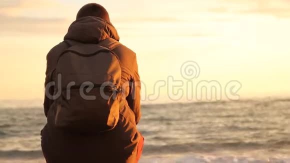 年轻男子背着背包坐在岸上望着大海的波涛视频的预览图