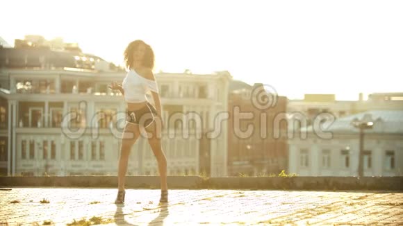 一位穿着小短裤的年轻女子在屋顶上表演迷人的性感舞蹈扮演她的臀部明亮的日落视频的预览图