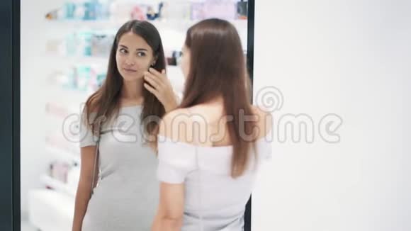 美丽的女孩在化妆品店的镜子前打扮自己慢动作视频的预览图