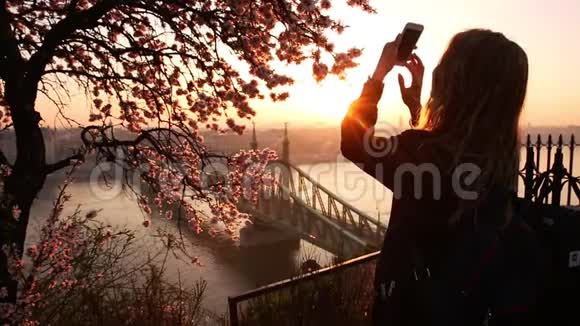 女游客在一部手机上拍照城市景观和多瑙河上的自由桥从露台上视频的预览图