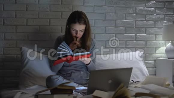 疲倦的学生女孩看书和笔记本电脑准备在卧室迟到的考试视频的预览图