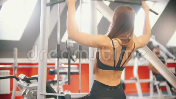 一位运动员女子在健身房训练坐着把杆拉到身体上训练双手视频的预览图
