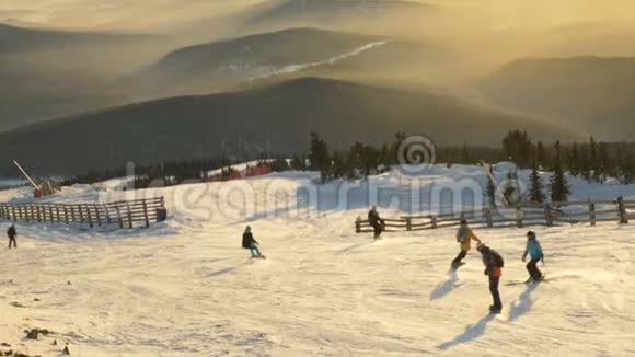 一群滑雪者和滑雪者在夕阳和山峦的映衬下走下滑雪坡视频的预览图