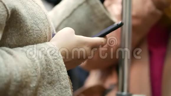 穿着浅色外套的年轻女子右手拿着地铁车里的一部黑色手机在智能手机上写消息视频的预览图