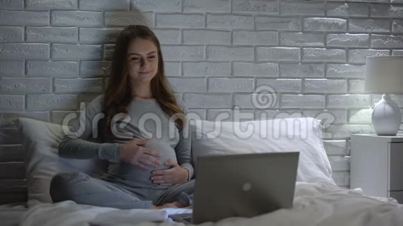快乐的孕妇抚摸肚子在网上观看教育视频视频的预览图