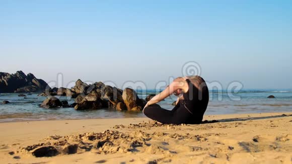 年轻女子在沙滩上练习瑜伽对抗褐色岩石视频的预览图