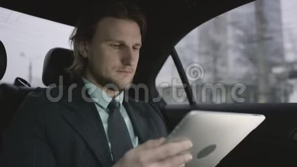 一个英俊的男人棕色头发穿着开心果衬衫穿着灰色西装坐在车用他的平板电脑工作视频的预览图