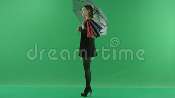 漂亮的年轻女子在购物后拿着袋子站在伞下颜色关键绿色背景视频的预览图