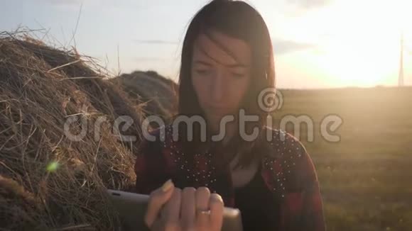 农民依靠干草用平板电脑在麦田上女农民在干草堆旁边的田里使用平板电脑微笑视频的预览图
