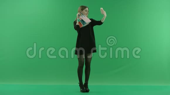 美丽的年轻女子用手机相机彩色钥匙绿色背景的礼品袋拍照视频的预览图