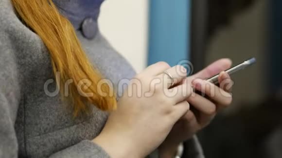 穿着浅色外套的年轻女子右手拿着地铁车里的一部黑色手机在智能手机上写消息视频的预览图