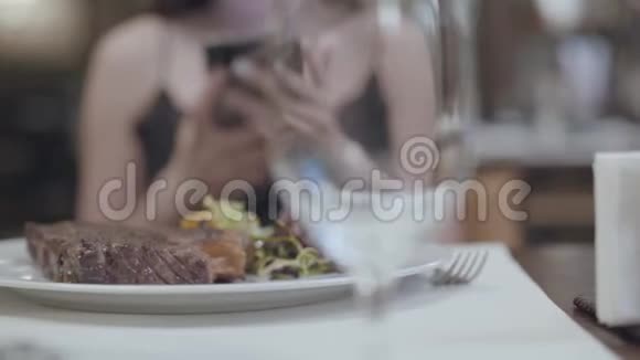 美味的牛排蔬菜和叶子躺在盘子里在餐厅的女人面前女士的手在发短信视频的预览图