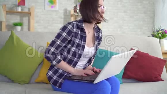 坐在沙发上用笔记本电脑工作的女人因为痔疮而感到疼痛和不适视频的预览图