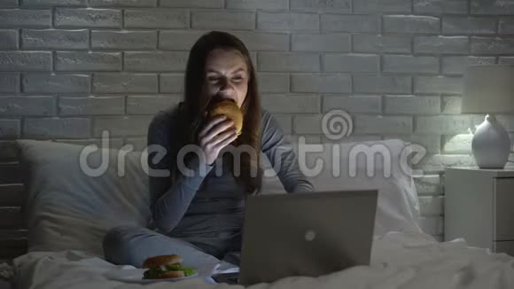 年轻女性在晚上上网时吃汉堡吃垃圾食品视频的预览图