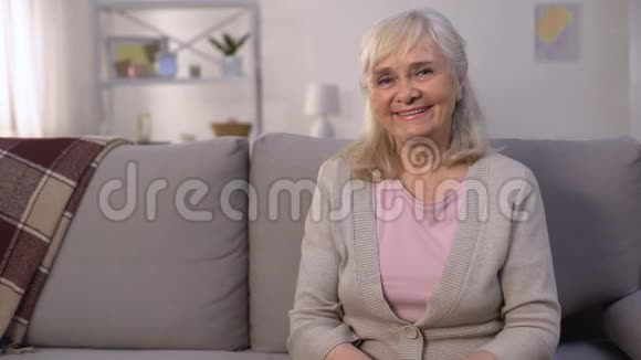 幸福健康的老妇人坐在客厅沙发上照相机前微笑视频的预览图