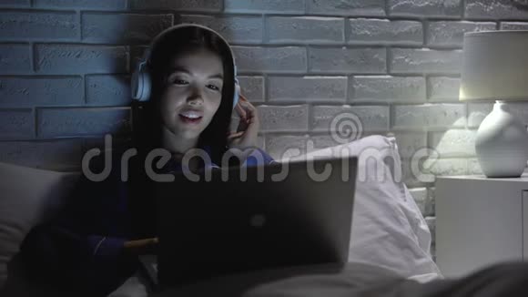 漂亮的亚洲女人晚上听耳机音乐欣赏最喜欢的歌曲视频的预览图
