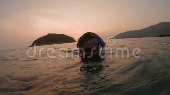 一个年轻男子潜水员在日落时在水中拍摄自拍视频的慢镜头水下航行器视频的预览图