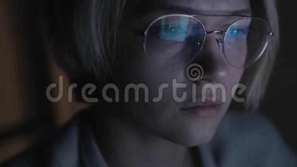 戴眼镜的年轻悲伤的女人在黑暗的房间里用电脑翻新闻视频的预览图