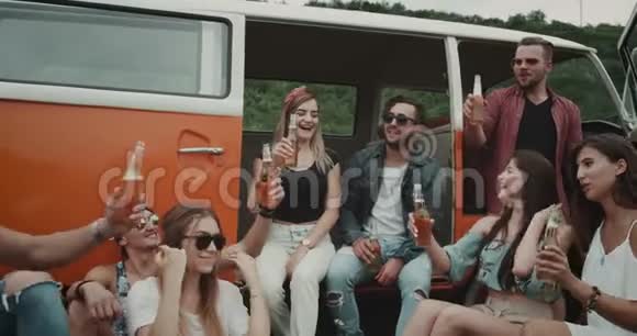 一群时髦的朋友在野餐聚会上喝着啤酒和欢呼声坐在复古的货车后面视频的预览图