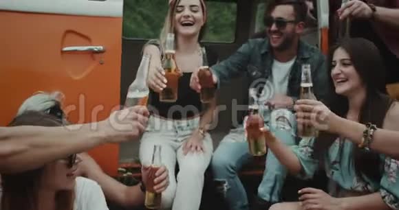 特写一群大朋友喝着啤酒彼此欢呼旁边有一辆复古的橙色面包车非常时尚的朋友视频的预览图