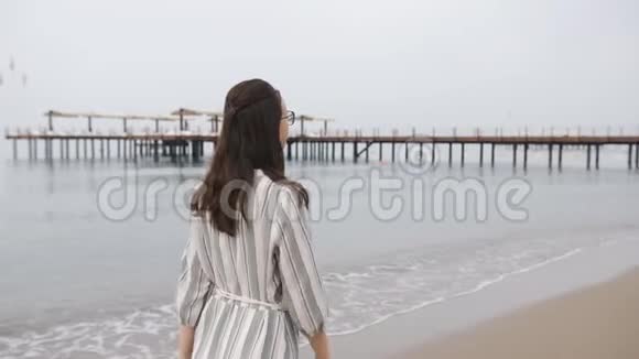 快乐的女人穿着一件长裙子光着脚在海滨散步笑着享受生活视频的预览图