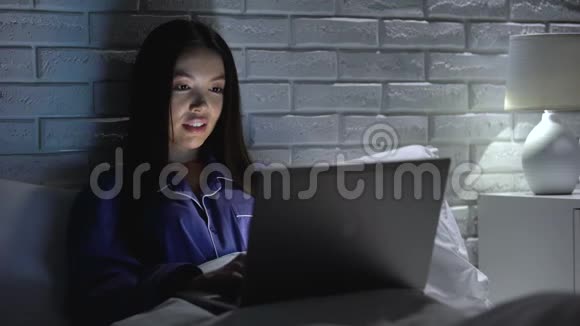 快乐的女人晚上在笔记本电脑上完成项目躺在床上加班视频的预览图