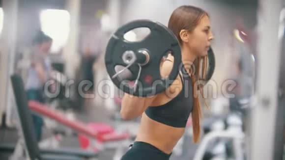 一位在健身房训练的女运动员肩膀上戴着哑铃蹲着视频的预览图