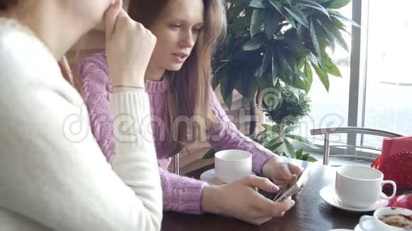 两个漂亮的女朋友正在社交媒体上谈论从智能手机屏幕到咖啡馆的咖啡休息时间的新闻视频的预览图