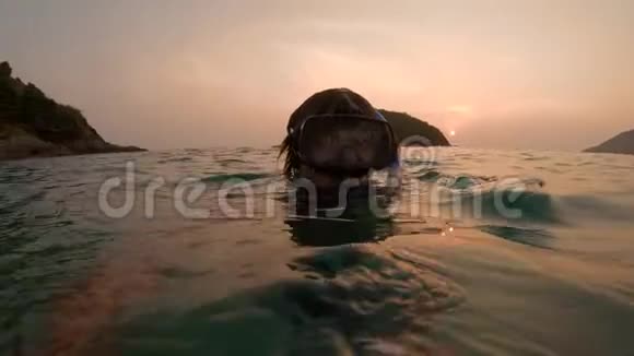 一个年轻男子潜水员在日落时在水中拍摄自拍视频的慢镜头水下航行器视频的预览图