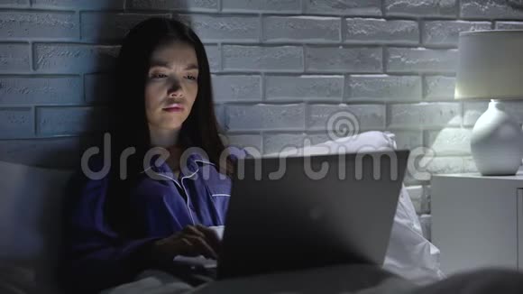 睡眠不足的女人晚上在床上用笔记本电脑工作在无聊的项目中没有动力视频的预览图