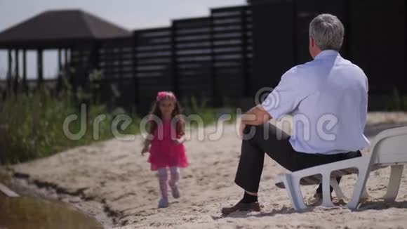 女孩跑向她的祖父拥抱他的脖子对着镜头微笑4K慢慢视频的预览图