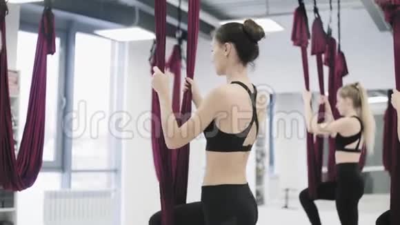 年轻美丽的瑜伽女性在健身俱乐部的红色吊床上做空中瑜伽练习视频的预览图