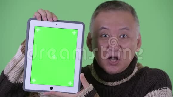 一脸快乐成熟的日本男人一边说话一边展示数字平板电脑视频的预览图